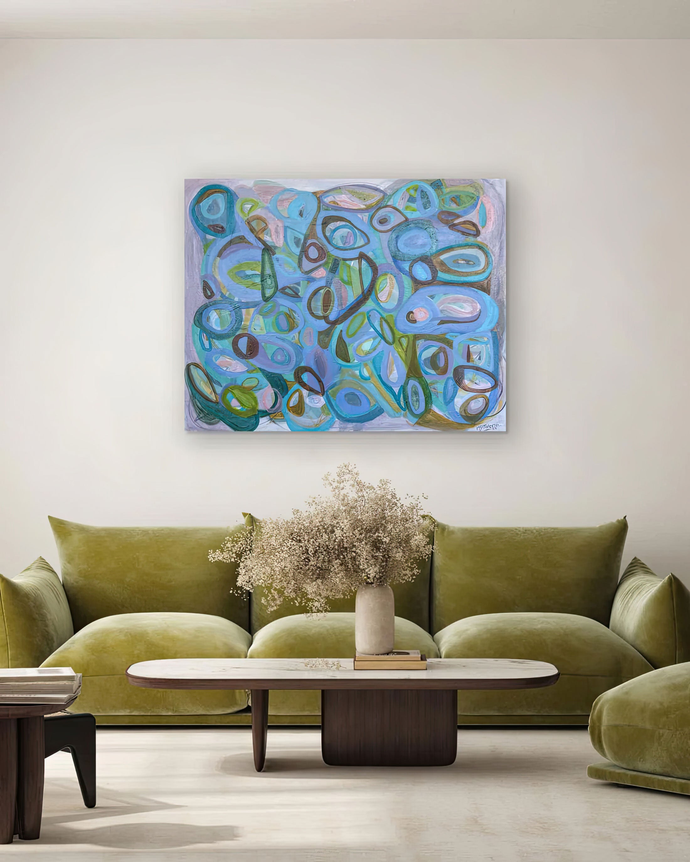 Abstract painting on a wall above a green sofa in a living room, Abstract artwork with circular shapes in blue, green, and brown on a white background, Gabriela Tolomei Fluir sostenido